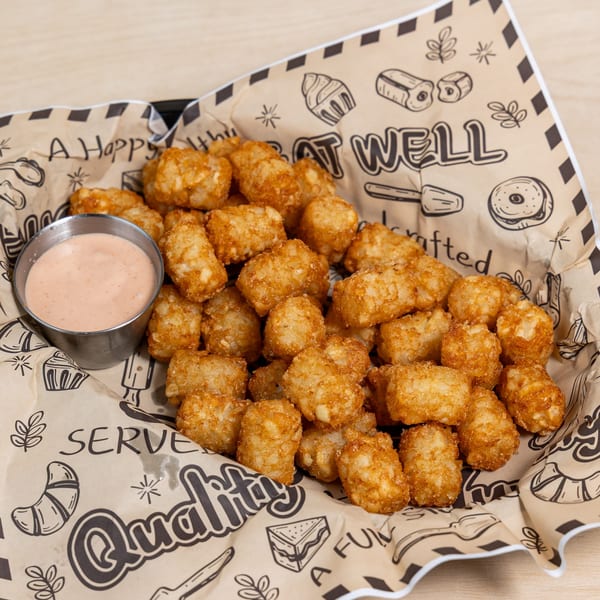 Golden brown tater tots in a paper-lined basket with a side of dipping sauce.