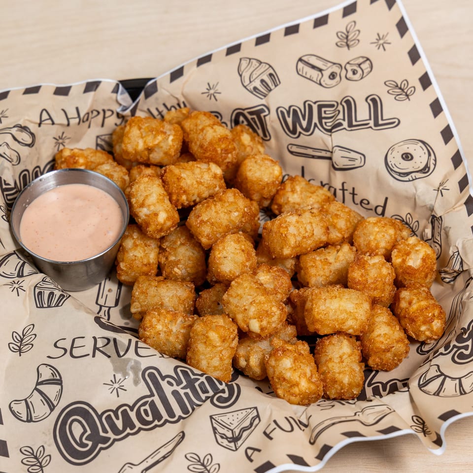 Golden brown tater tots in a paper-lined basket with a side of dipping sauce.