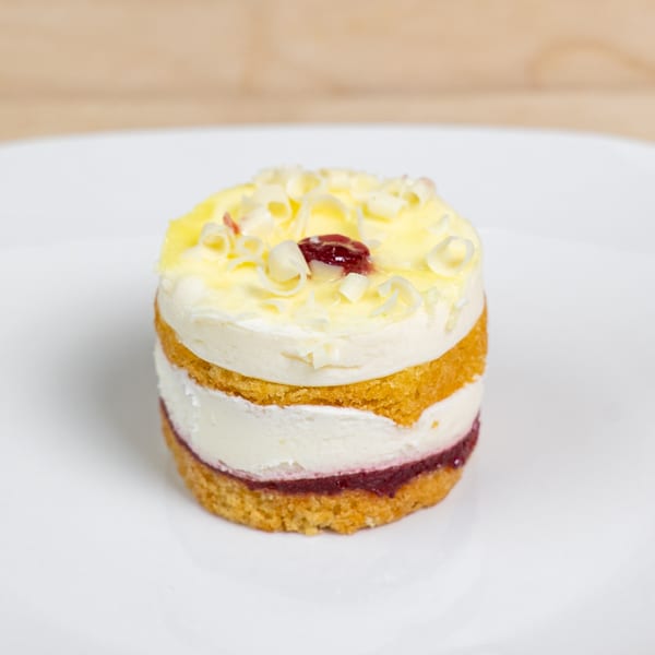 A layered dessert with yellow cake, white cream, and red jam, topped with white chocolate curls.