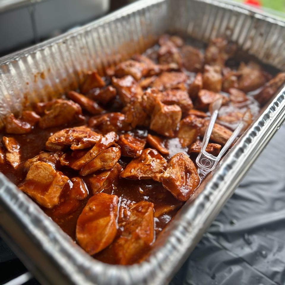 Close-up of barbecue chicken pieces in a foil pan with serving tongs at Townline Grill.