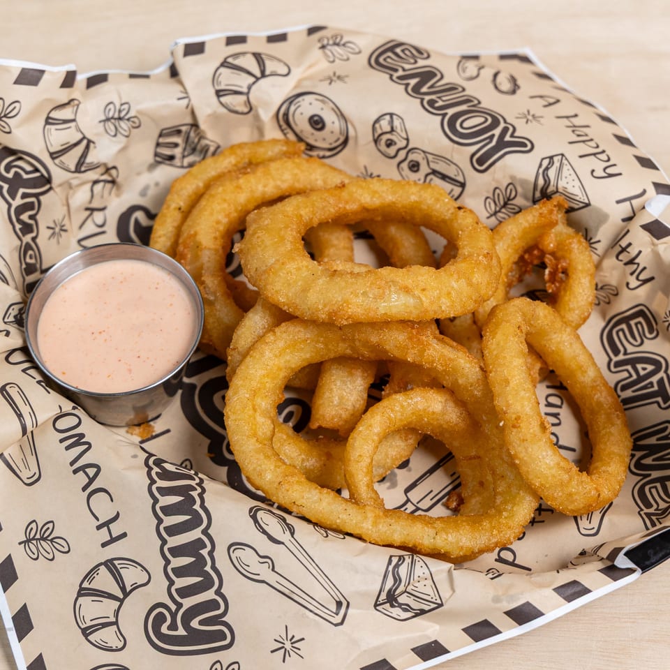 Golden-brown onion rings with a side of dipping sauce, served in a paper-lined basket.