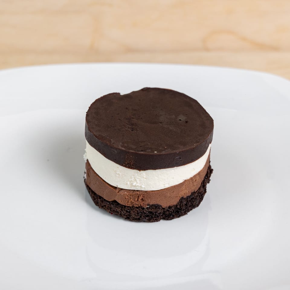 A layered chocolate dessert with dark chocolate, white, and milk chocolate mousse on a white plate.